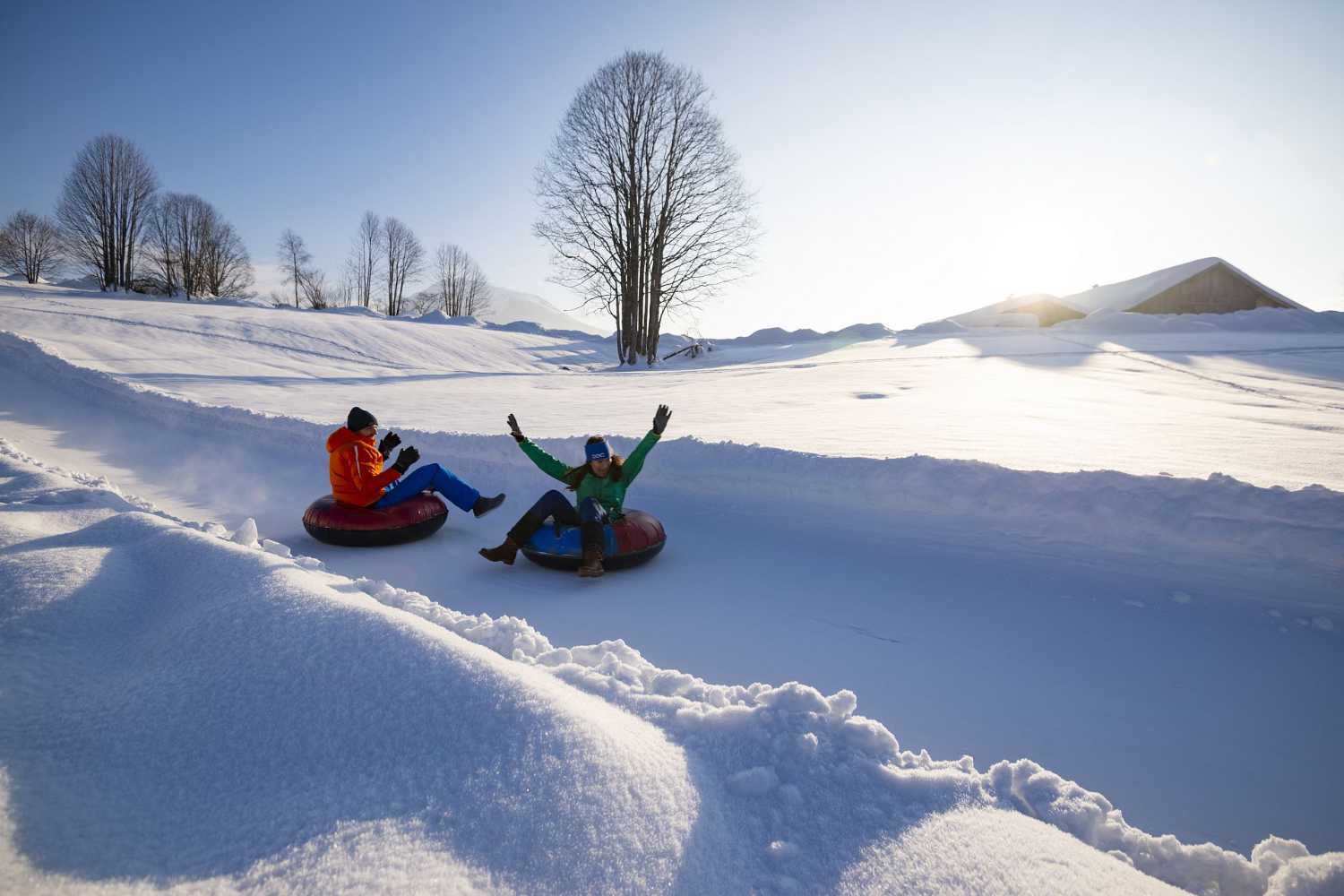 Kinder beim Snowtubing auf präparierter Bahn im Kaiserwinkl in Tirol bei Wintersonne