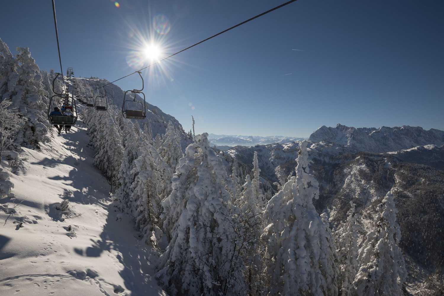 Sessellift über verschneiten Bäumen mit Bergpanorama und Wintersonne im Kaiserwinkl