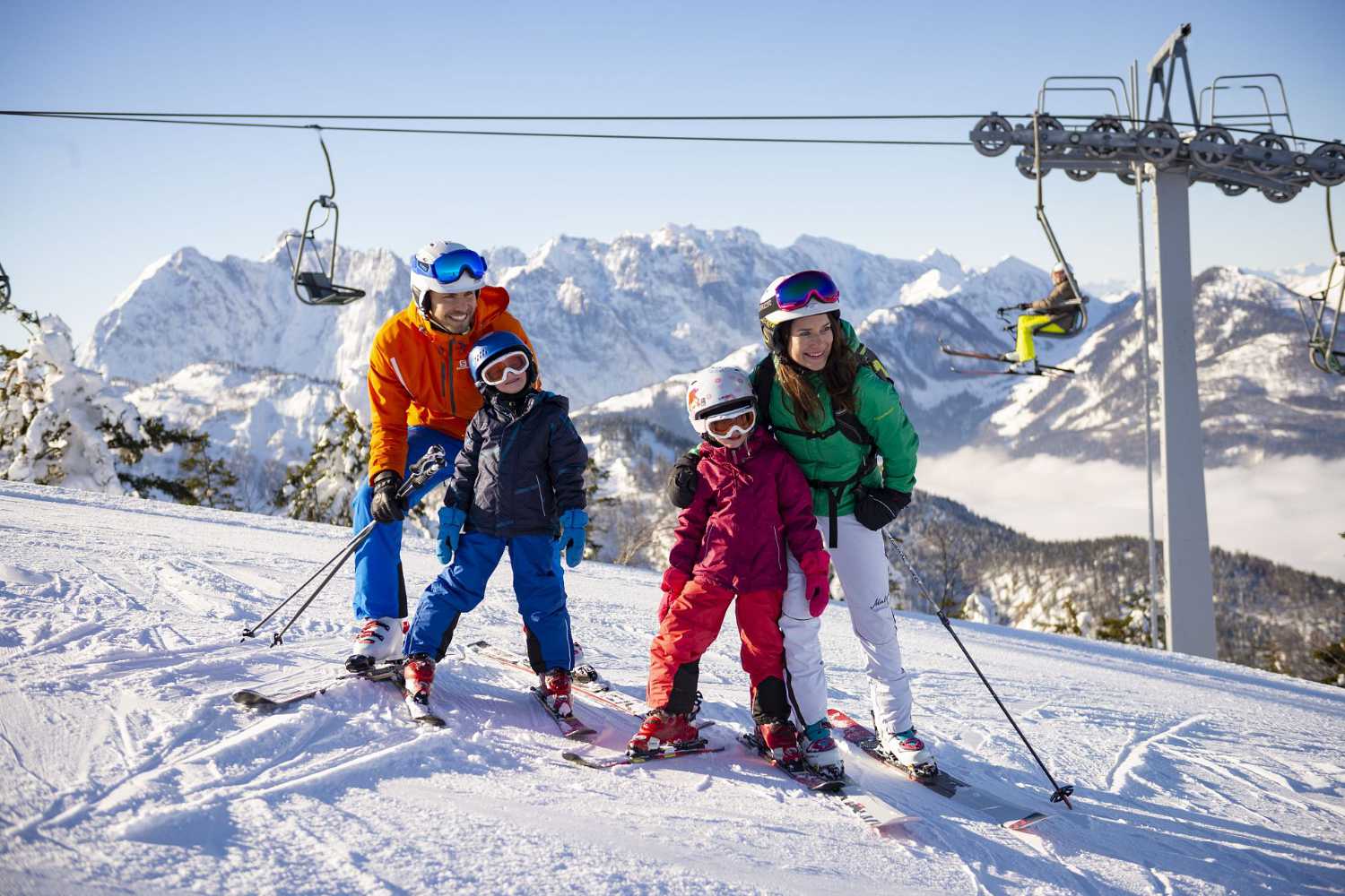 Familie mit Kindern auf der Skipiste nahe Liftanlage mit Bergpanorama im Kaiserwinkl