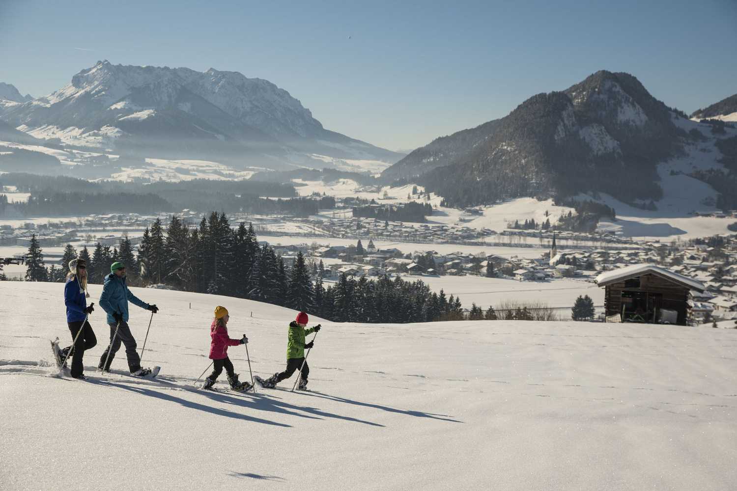 Familie beim Winterwandern im Kaiserwinkl in Tirol mit verschneiten Wiesen und Bergpanorama