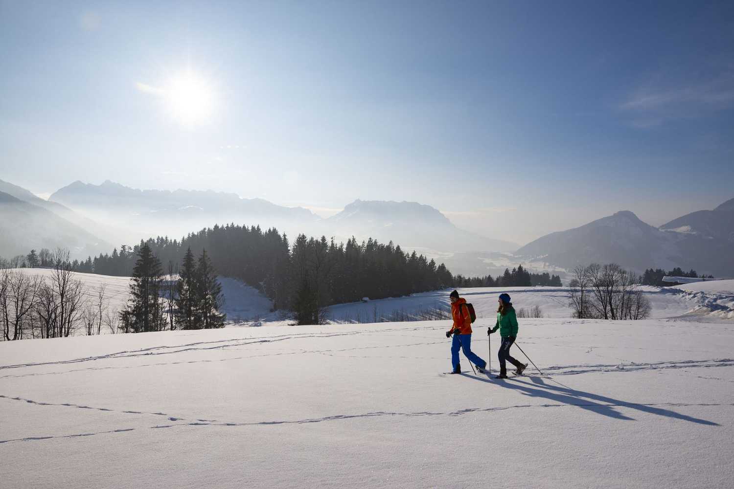 Zwei Winterwanderer auf verschneiter Landschaft mit Sonne und Bergblick im Kaiserwinkl nahe Schwendt